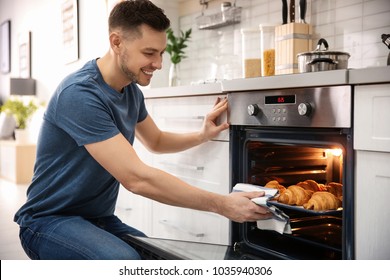 Man taking baking tray with delicious croissants out of electric oven in kitchen