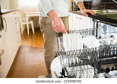 A man taking clean dishes out of dishwasher. Person doing household chores in the kitchen, unloading dish washing machine. The man is doing daily home routine. Modern interior with kitchen appliances - Powered by Shutterstock