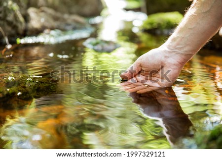 Man taking clear water from a stream in forest. Close-up hand. Nuuksio National Park, Finland. Sunny summer day in forest. Beautiful spring water running in rocks. 