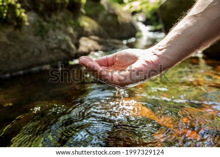 Man taking clear water from a stream in forest. Close-up hand. Nuuksio National Park, Finland. Sunny summer day in forest. Beautiful spring water running in rocks. 