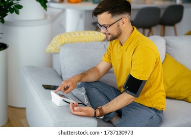 Man Taking His Blood Pressure At Home In The Living Room On Sofa.