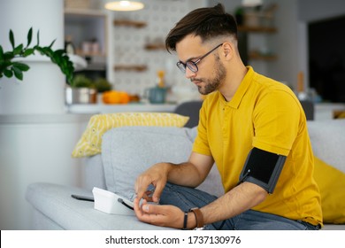 Man Taking His Blood Pressure At Home In The Living Room On Sofa.