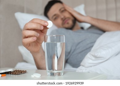 Man Taking Medicine For Hangover In Bed At Home, Focus On Hand With Pill