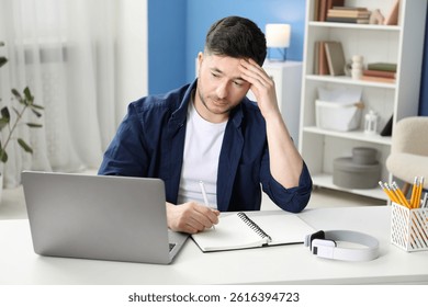 Man taking notes during online lesson at desk indoors. Self-study