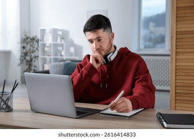 Man taking notes during online lesson at desk indoors. Self-study