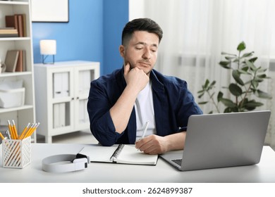 Man taking notes during online lesson at desk indoors. Self-study