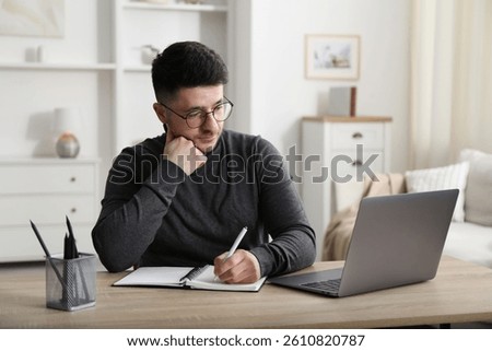 Man taking notes during online lesson at desk indoors. Self-study