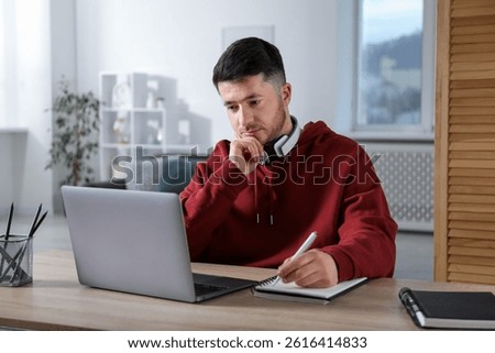 Man taking notes during online lesson at desk indoors. Self-study