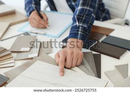 Man taking notes at table with different samples of wooden flooring indoors, closeup