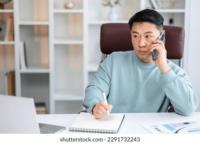 man Taking Notes While Having Phone Conversation, Sitting At Desk In Modern Office Talking On Cellphone With Client. Copy space