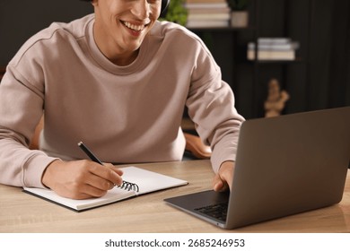 Man taking notes while passing online test via laptop at table indoors, closeup
