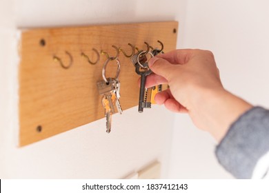 Man taking an old door key from wooden key holder hanging on the white wall, close up shot of male's hand
