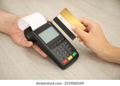 Man taking payment from client via credit card terminal at wooden table, closeup