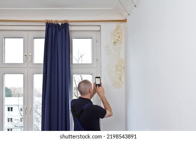 Man taking a photo of a big patch of mold or mildew growing behind the drapes of a white external wall in an old house.