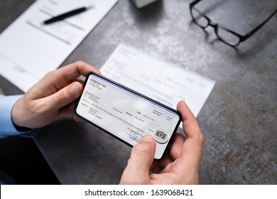 Man Taking Photo Of Cheque To Make Remote Deposit In Bank