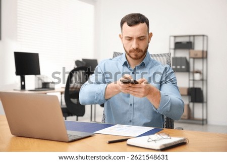 Man taking photo of document using scanning app on smartphone at desk in office