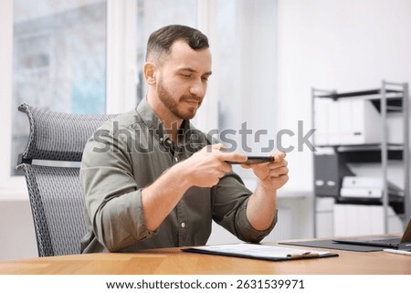 Man taking photo of document using scanning app on smartphone at desk in office