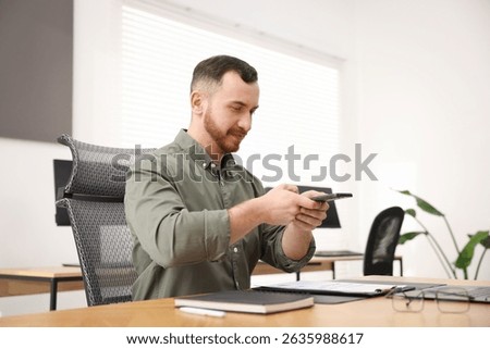 Man taking photo of document using scanning app on smartphone at desk in office