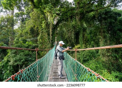 Man taking photo with at suspension bridge in tree top canopy walkway in Danum rain forest Lahad Datu Sabah Borneo - Shutterstock ID 2236098777