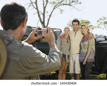 Man taking photograph of three friends against jeep