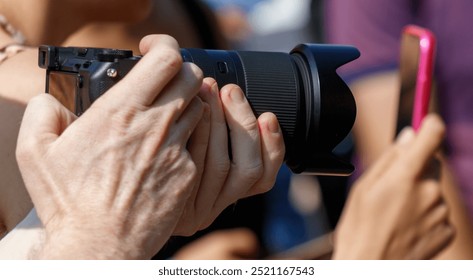 A man is taking a picture with a camera while another person is holding a pink phone. The scene seems to be casual and relaxed, with the man taking a photo and the other person holding a phone