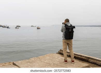 A man is taking a picture of the ocean with his camera. The sky is cloudy and the water is calm