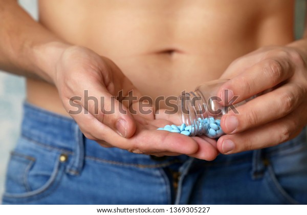 Man taking pills, bottle with blue tablets in male
hands close up. Muscular guy in unzipped jeans with naked torso,
concept of viagra, medication for stomach, erection, sleeping or
digestive pill