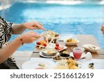 Man taking salad with fork by poolside breakfast table