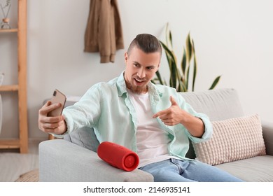 Man Taking Selfie With Modern Wireless Portable Speaker On Sofa In Light Room