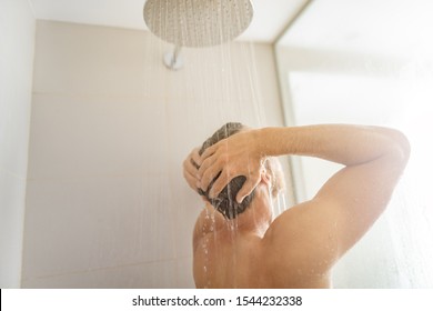 Man taking a shower washing hair under water falling from rain showerhead in luxury walk-in bath. Showering young person at home lifestyle. Body care morning routine in sunlight. - Powered by Shutterstock