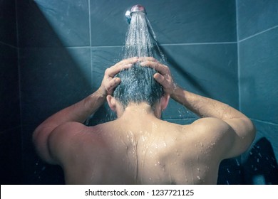 Man taking a showeron a beautiful blue bathroom washing hair and body under water falling from rain showerhead. Showering person at home lifestyle. Young adult body care morning routine.
