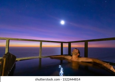 Man taking Some leisure time with a bath in a wooden hot tub with amazing views over the Pacific Ocean during an awe sunset. Idyllic scenery for some relaxation time during holidays at Chile coast