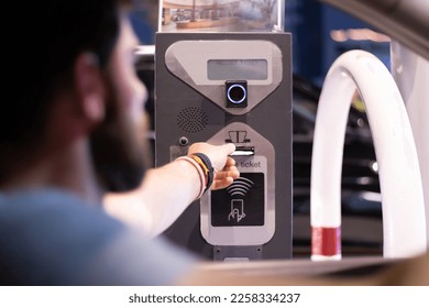 man taking ticket to pass control on parking area, man getting ticket from parking meter barrier. young adult taking a parking ticket from a machine trough the car's window