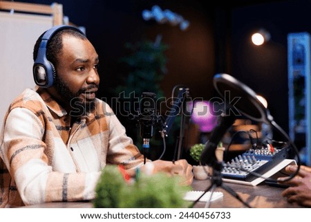 Man talk show host using audio equipment and having a friendly interview with an upcoming artist at home studio. African american content creator with headphones and microphone is creating a podcast.