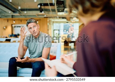 Man talking and gesturing while therapist is listening, writing notes during a professional mental health consultation