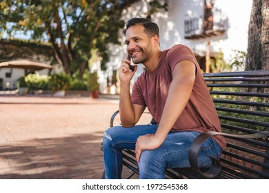 Man Talking On The Cell Phone, Showing Happiness Sitting On A Bench In The Colonial City Of Santo Domingo