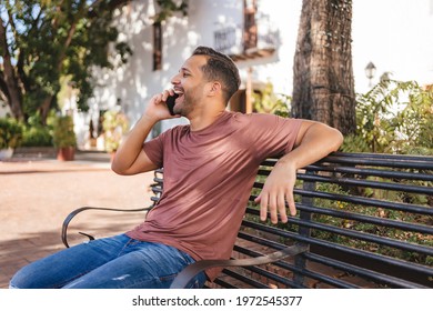 Man Talking On The Cell Phone, Showing Happiness Sitting On A Bench In The Colonial City Of Santo Domingo