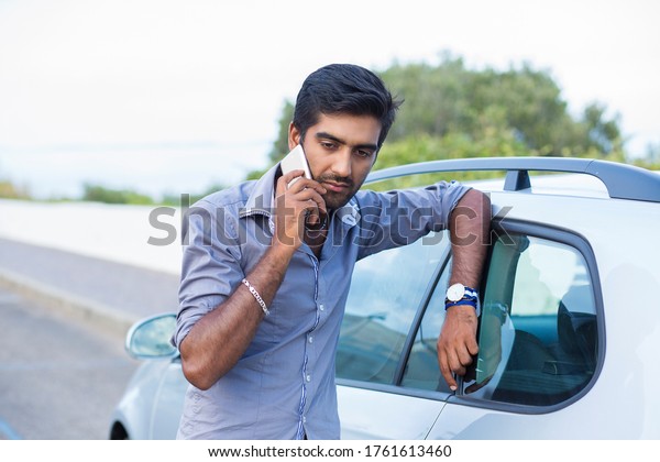Man talking\
on a cell phone leaning on the door of his car angry unhappy sad\
displeased with the\
conversation