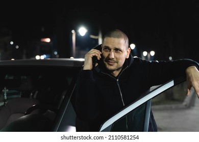 A Man Talking On His Phone Outside At Night Leaning On His Car