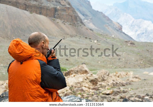 Man\
Talking on Radio.\
Mountain Rescue Officer Holding Radio Walkies\
Talkie and Severe Mountain Landscape\
Background