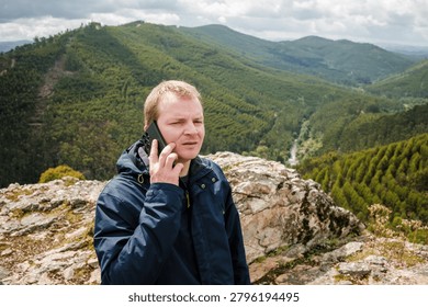 Man talking on a smartphone while standing on a rocky mountain overlooking a vast forest