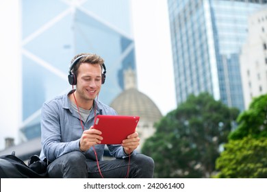 Man Talking On Tablet Pc Having Video Chat Conversation In Sitting Outside Using App On 4g Wireless Device Wearing Headphones. Casual Young Urban Professional Male In His Late 20s. Hong Kong.