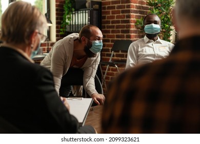 Man Talking To People At Aa Group Meeting About Mental Health, Having Face Mask. Multi Ethnic Patients With Addiction Attending Therapy Session And Having Conversation About Problems.