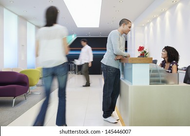 Man Talking To Receptionist At The Reception Desk In Office