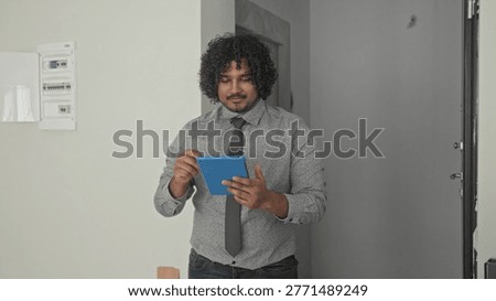 Man tapping blue tablet with hands inside a building during an empty house walkthrough; confidence property viewing.
