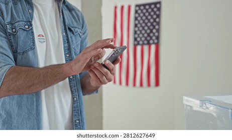 Man tapping smartphone with hands by ballot box and 'i voted' sticker in polling building; civic pride.