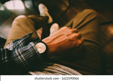 The man in tartan shirt sitting on chair wears a tartan shirt looking at his analog watch on his hand watching the time at the coffee shop. waiting for an appointment.