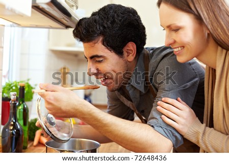 Man tasting soup on a stove in kitchen while happy woman is watching