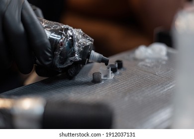 Man Tattoo Artist In Black Gloves Holds A Bottle Of Paint And Pours, Close-up. Tattoo Preparation Process