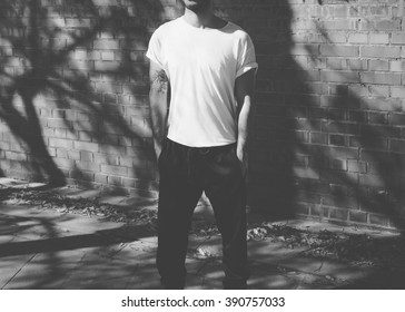 Man With Tattoo Wearing Blank White Tshirt, Sunglasses. Stands In Front Of A Brick Wall. City Street Background. Horizontal Mockup. Black, White